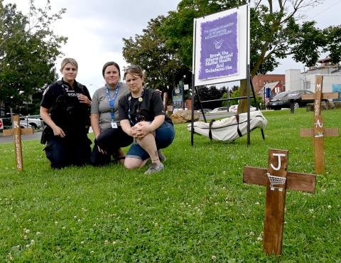 RN Amber Gilmour (centre) sits with law enforcement and outreach colleagues amongst several crosses representing residents lost to mental illness and substance use. Photo credit: Republished with the express permission of Brockville Recorder and Times, a division of Postmedia Network Inc. RN Amber Gilmour (centre) sits with law enforcement and outreach colleagues amongst several crosses representing residents lost to mental illness and substance use. Photo credit: Republished with the express permission of Brockville Recorder and Times, a division of Postmedia Network Inc.