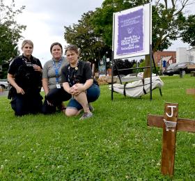 RN Amber Gilmour (centre) sits with law enforcement and outreach colleagues amongst several crosses representing residents lost to mental illness and substance use. Photo credit: Republished with the express permission of Brockville Recorder and Times, a division of Postmedia Network Inc.